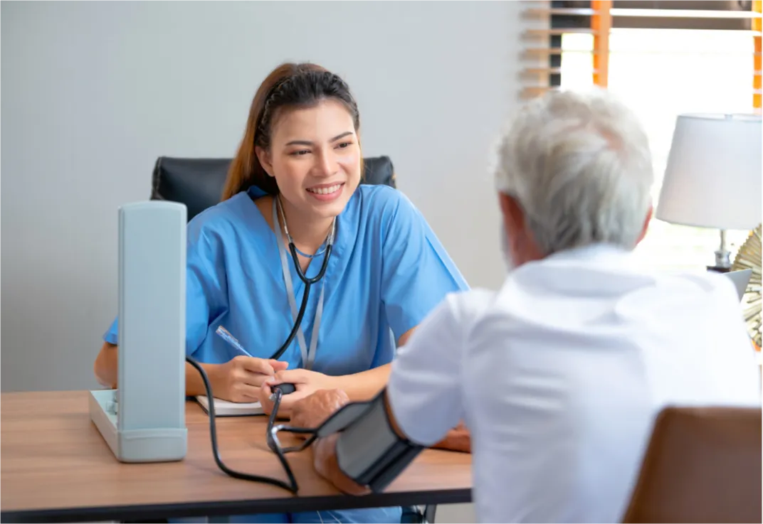 A healthcare professional smiles while taking notes and checking a patient's blood pressure in an office.