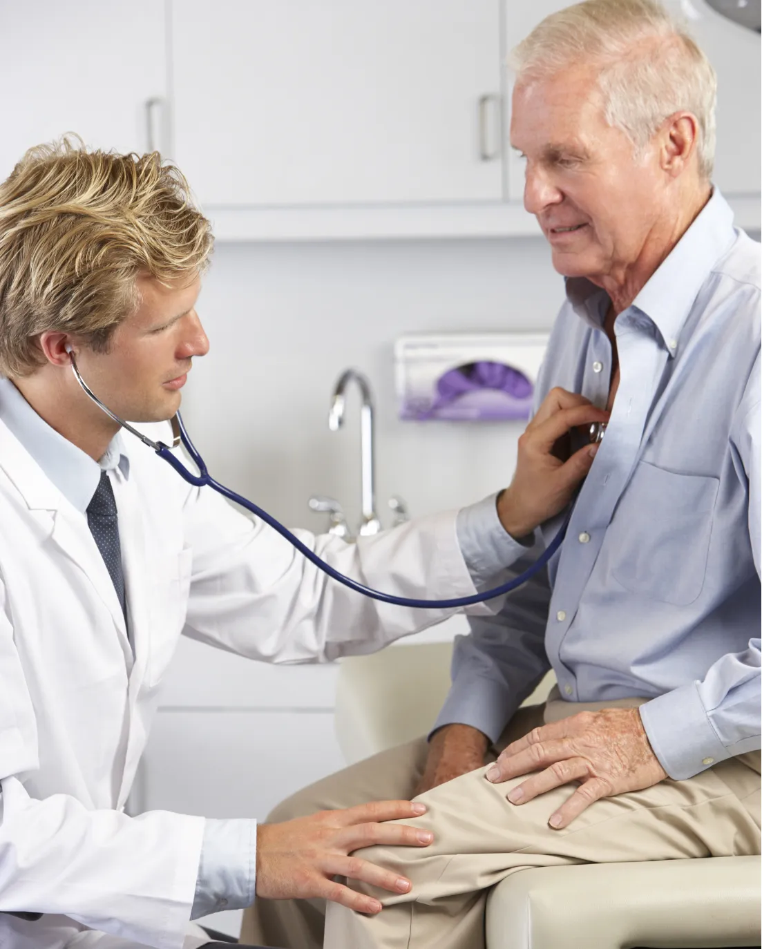 Doctor examining an elderly man's heart with a stethoscope in a medical office.