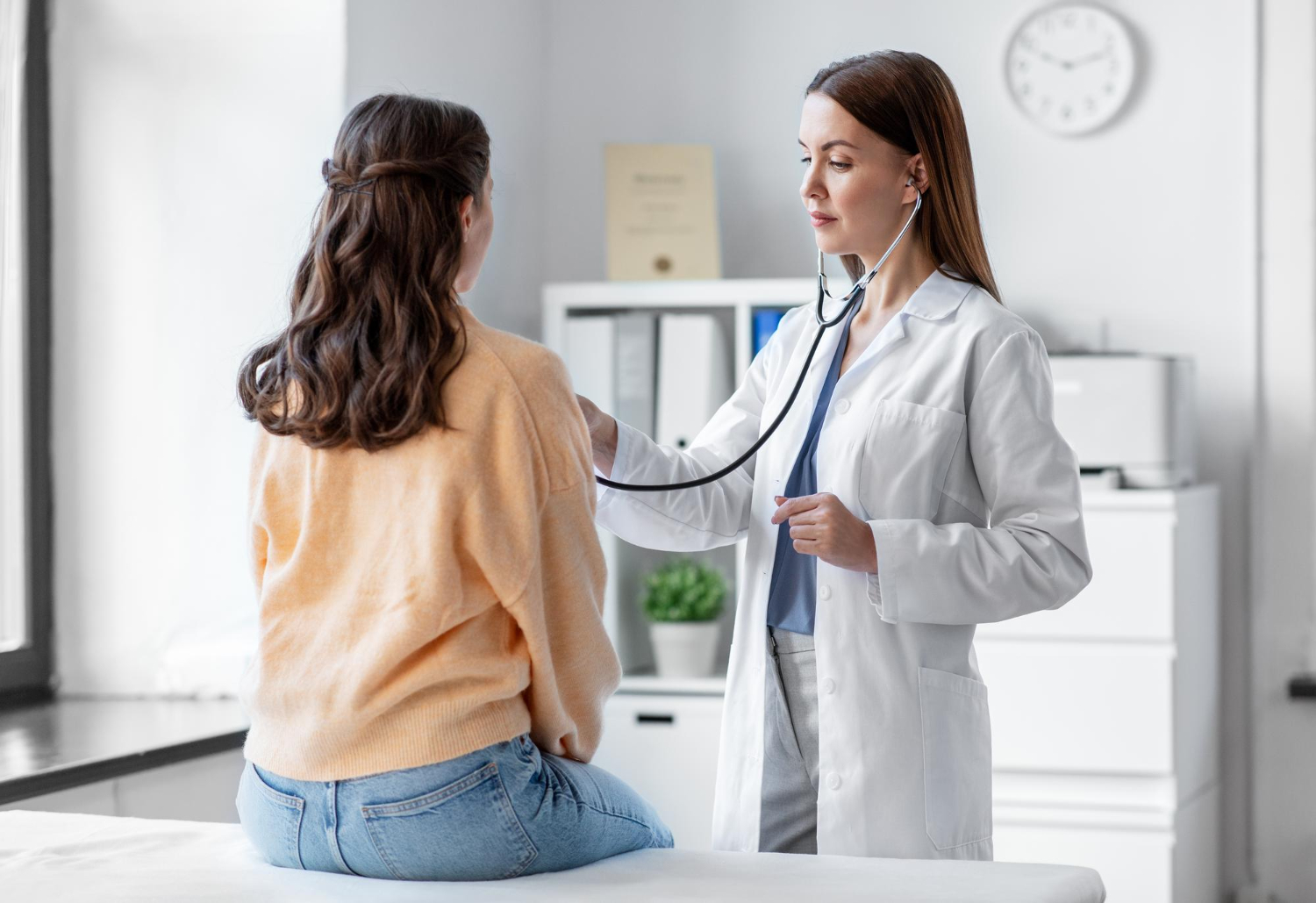 Doctor using a stethoscope to check a patient's heartbeat in a medical office.