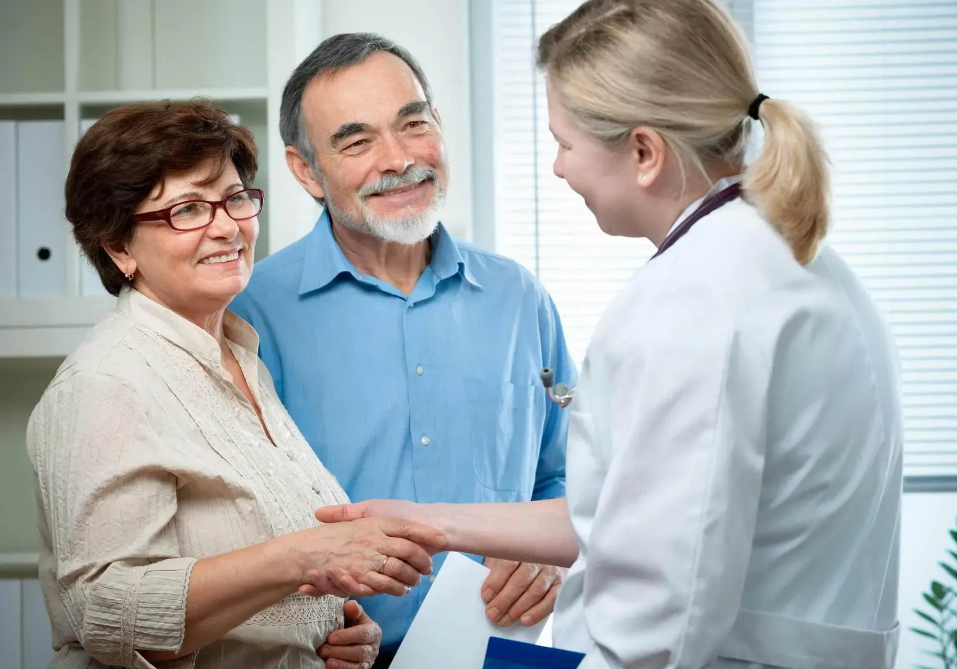 Smiling older couple shakes hands with a doctor in an office setting.