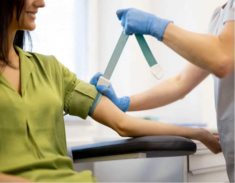 A healthcare worker puts a tourniquet on a woman's arm, preparing for a blood draw in a clinic.